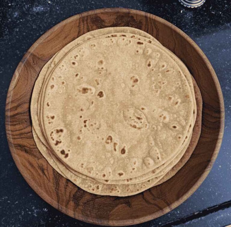 Freshly cooked soft chapathis stacked in a wooden plate.