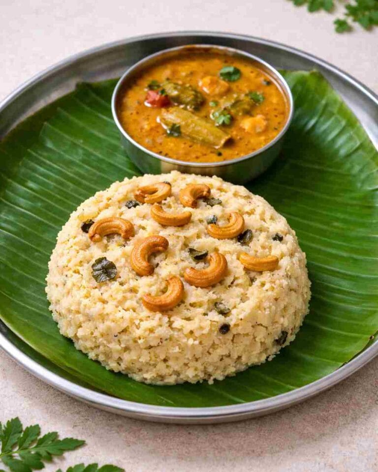 Ven Pongal served on a banana leaf with roasted cashews and a bowl of sambar