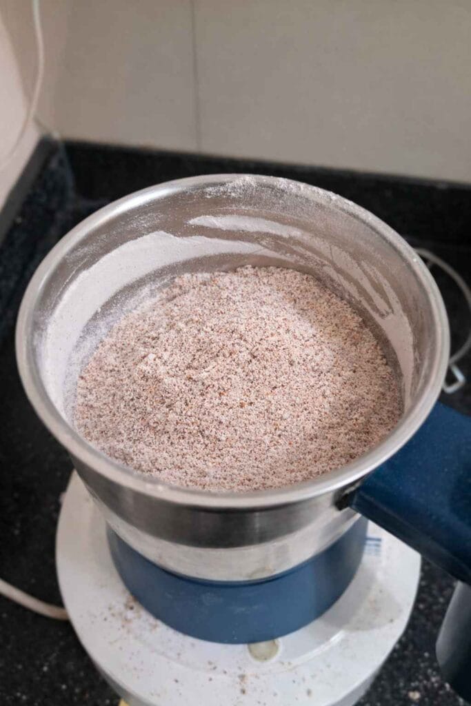 Grinding dried whole ragi in a mixer grinder to make ragi powder at home