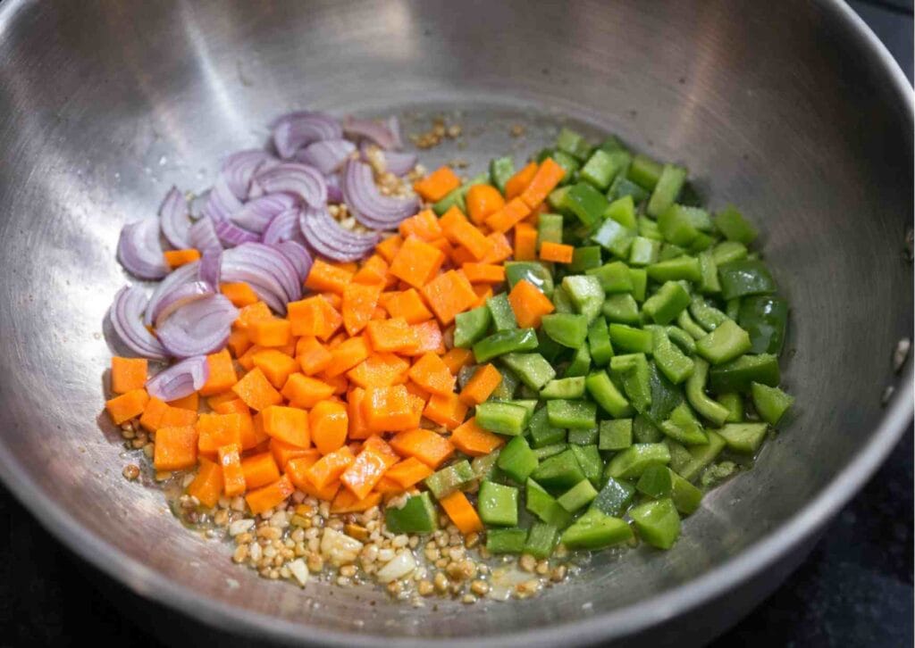 Chopped onion, carrot, and capsicum sauteing in a pan for quick egg fried rice recipe