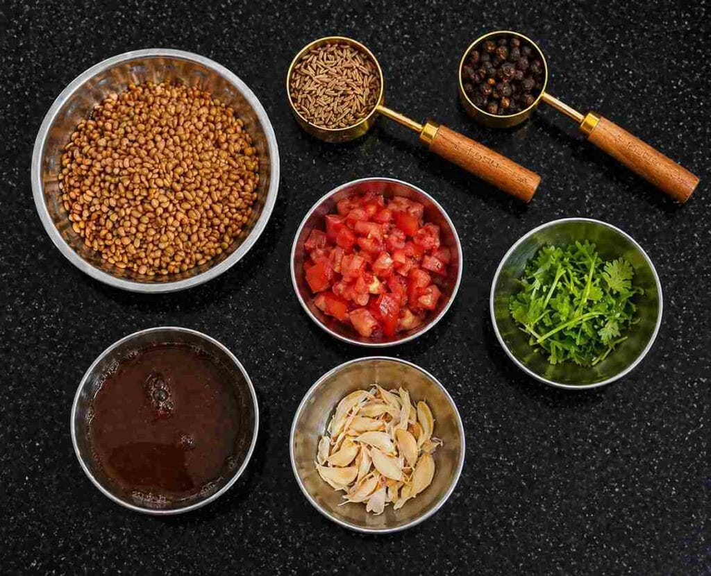 Kollu rasam ingredients including horse gram, cumin seeds, black pepper, tomatoes, garlic, tamarind extract, and coriander leaves