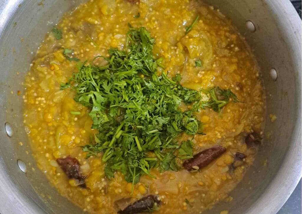 Cooked dal with ridge gourd and brinjal topped with fresh coriander leaves in a pressure cooker