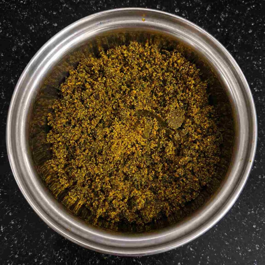 Homemade karuveppilai podi made with roasted curry leaves, dal, pepper, and sesame seeds in a steel bowl.