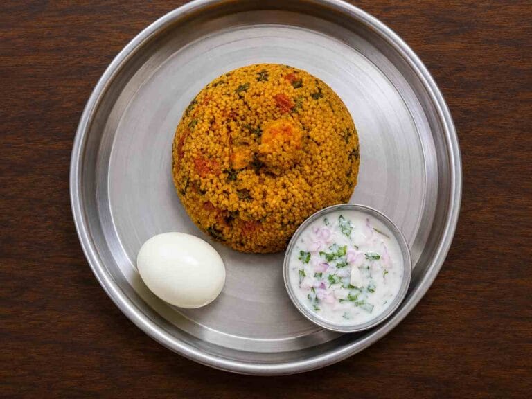 Varagu arisi prawn biryani served with onion raita and boiled egg on steel plate