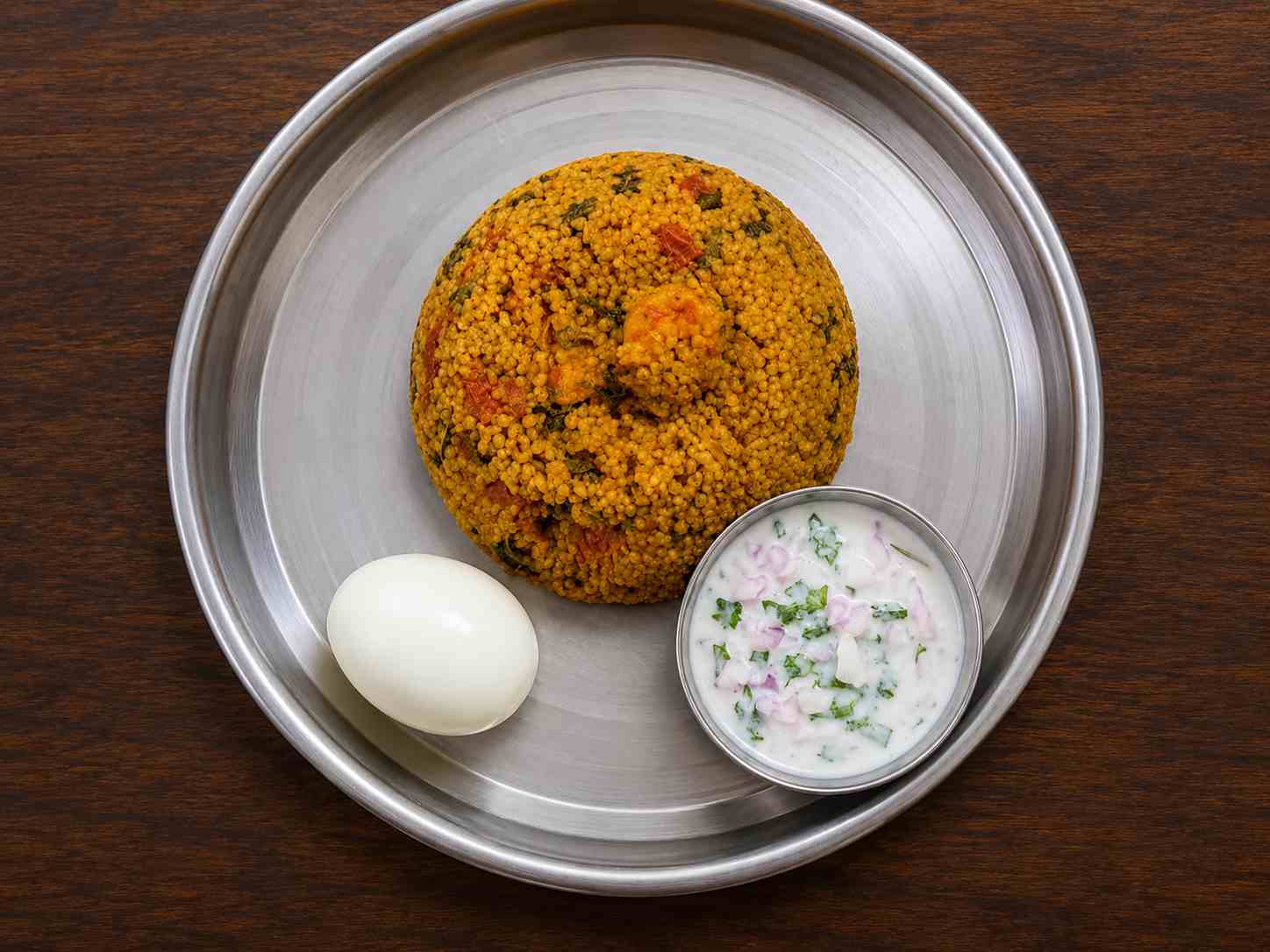 Varagu arisi prawn biryani served with onion raita and boiled egg on steel plate