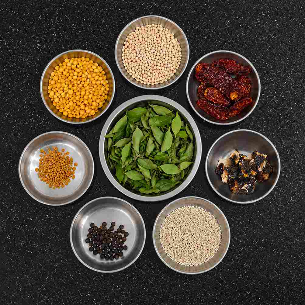Ingredients used for making Karuveppilai Sadam including curry leaves, urad dal, channa dal, red chilli, pepper, tamarind, and sesame seeds.