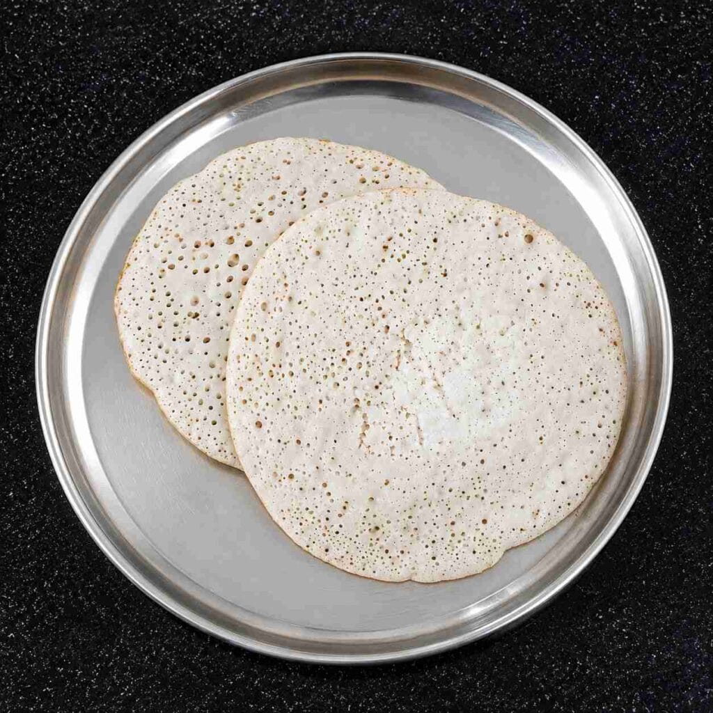 Soft and spongy coconut dosa served on plate with porous texture and fluffy center.