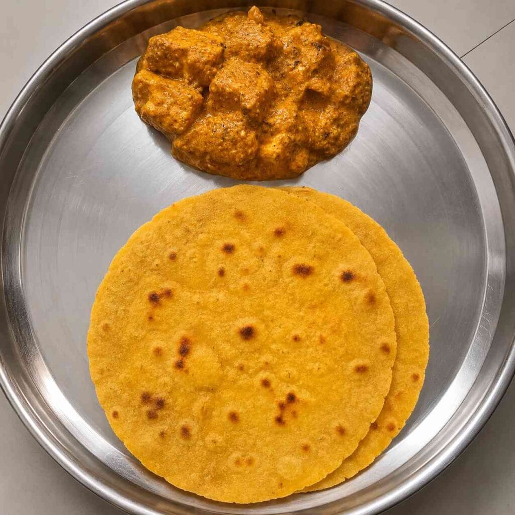 Soft homemade makki atta roti served with paneer curry on a steel plate