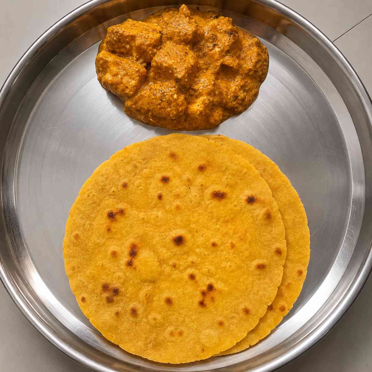 Soft homemade makki atta roti served with paneer curry on a steel plate