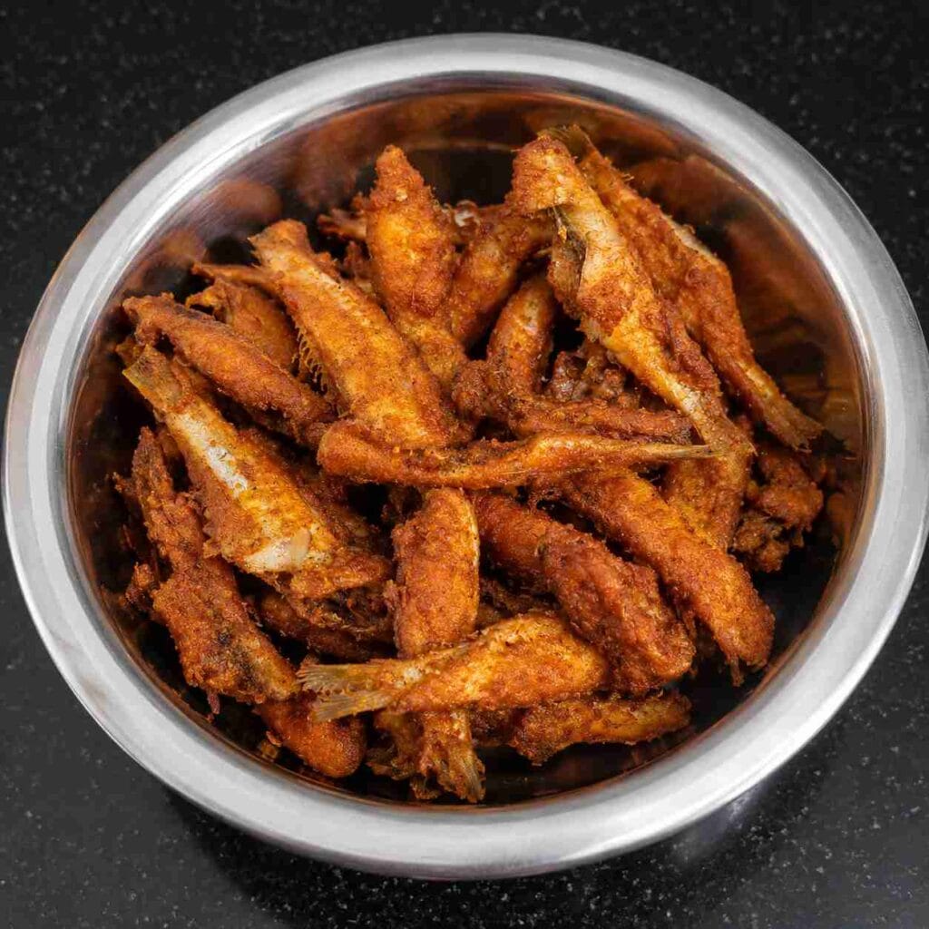 Crispy golden brown nethili fish fry served on a white plate with spicy homemade masala coating.