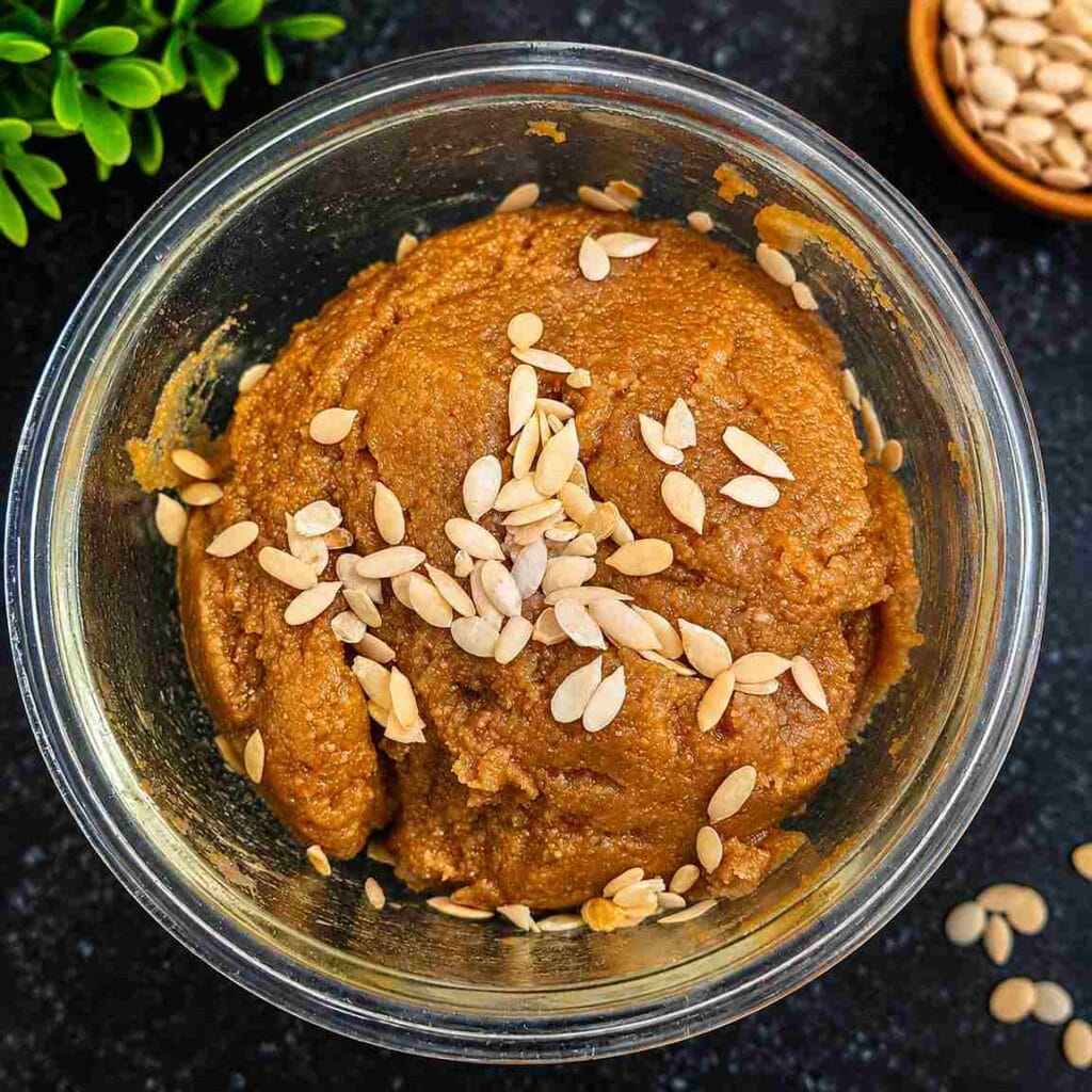 Chettinad Kummayam served in a glass bowl, garnished with pumpkin seeds, showing its rich brown colour and smooth texture.