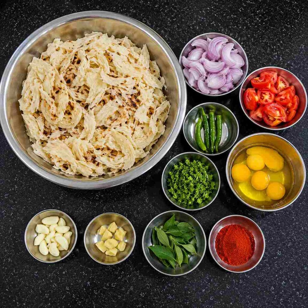 Shredded parottas with eggs, sliced onions, tomatoes, green chilies, garlic, ginger, curry leaves, coriander, and chili powder in bowls.
