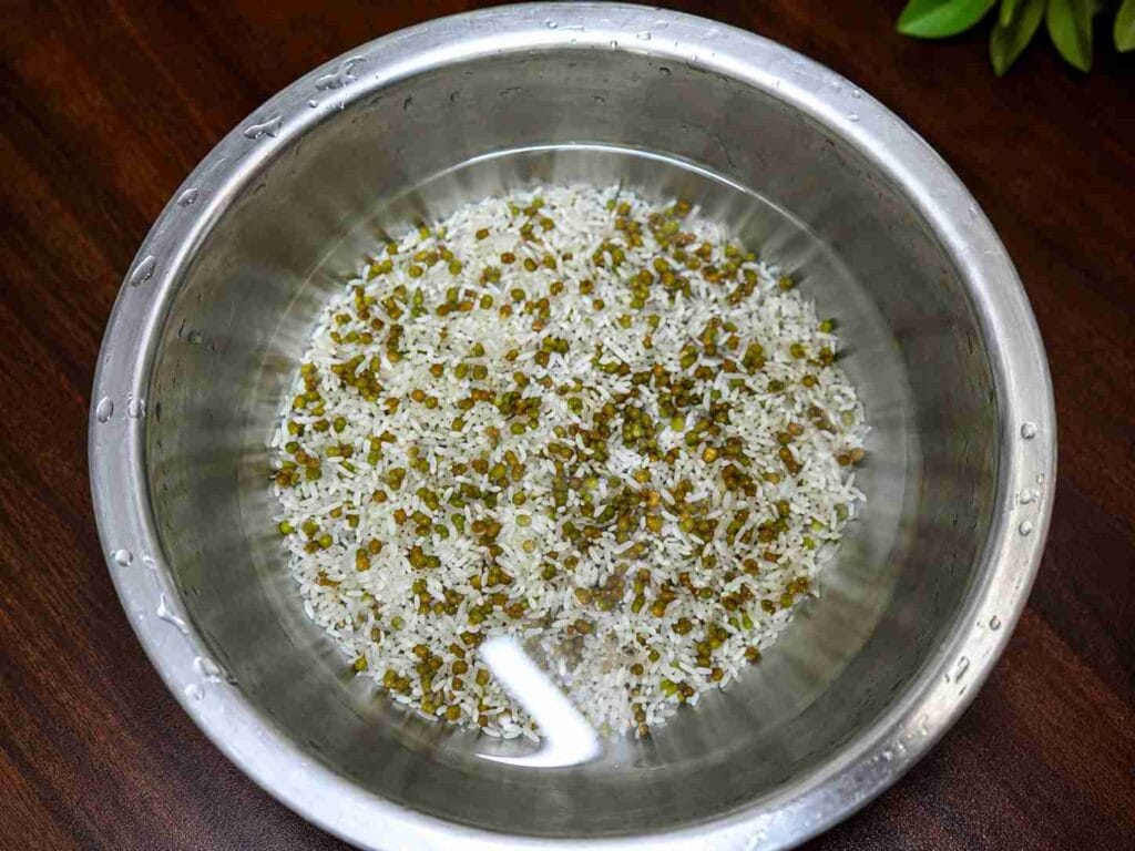 Whole green gram and raw rice soaking in water in a stainless steel bowl before cooking a healthy porridge.