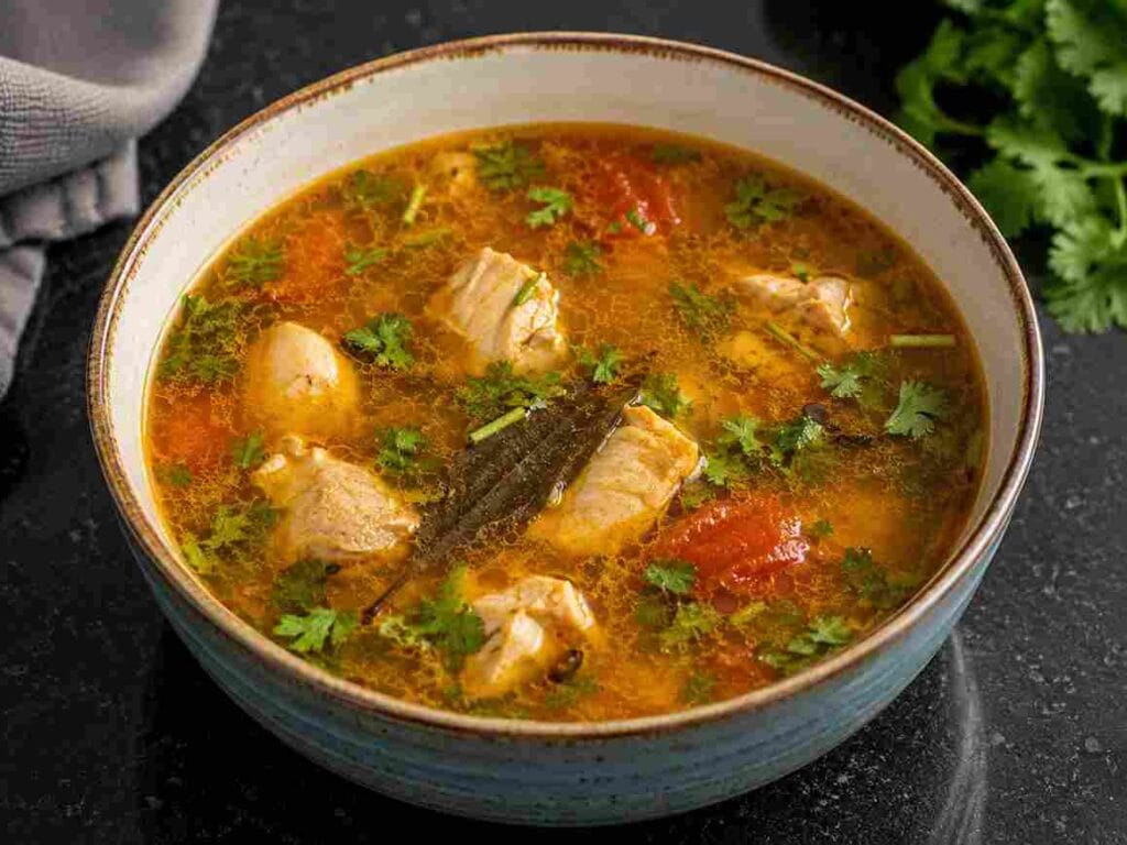 Bowl of homemade Chicken Pepper Soup with tender chicken pieces, tomato, bay leaf, coriander leaves, and pepper broth.