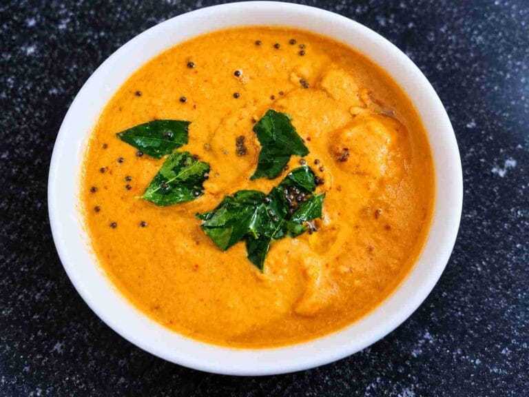 A bowl of Tomato Garlic Chutney topped with mustard seeds and fresh curry leaves, served as a South Indian chutney for idli and dosa.