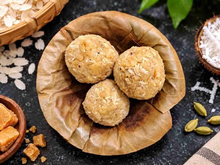 Three round Aval Laddus served on a leaf plate with poha, coconut and cardamom around them