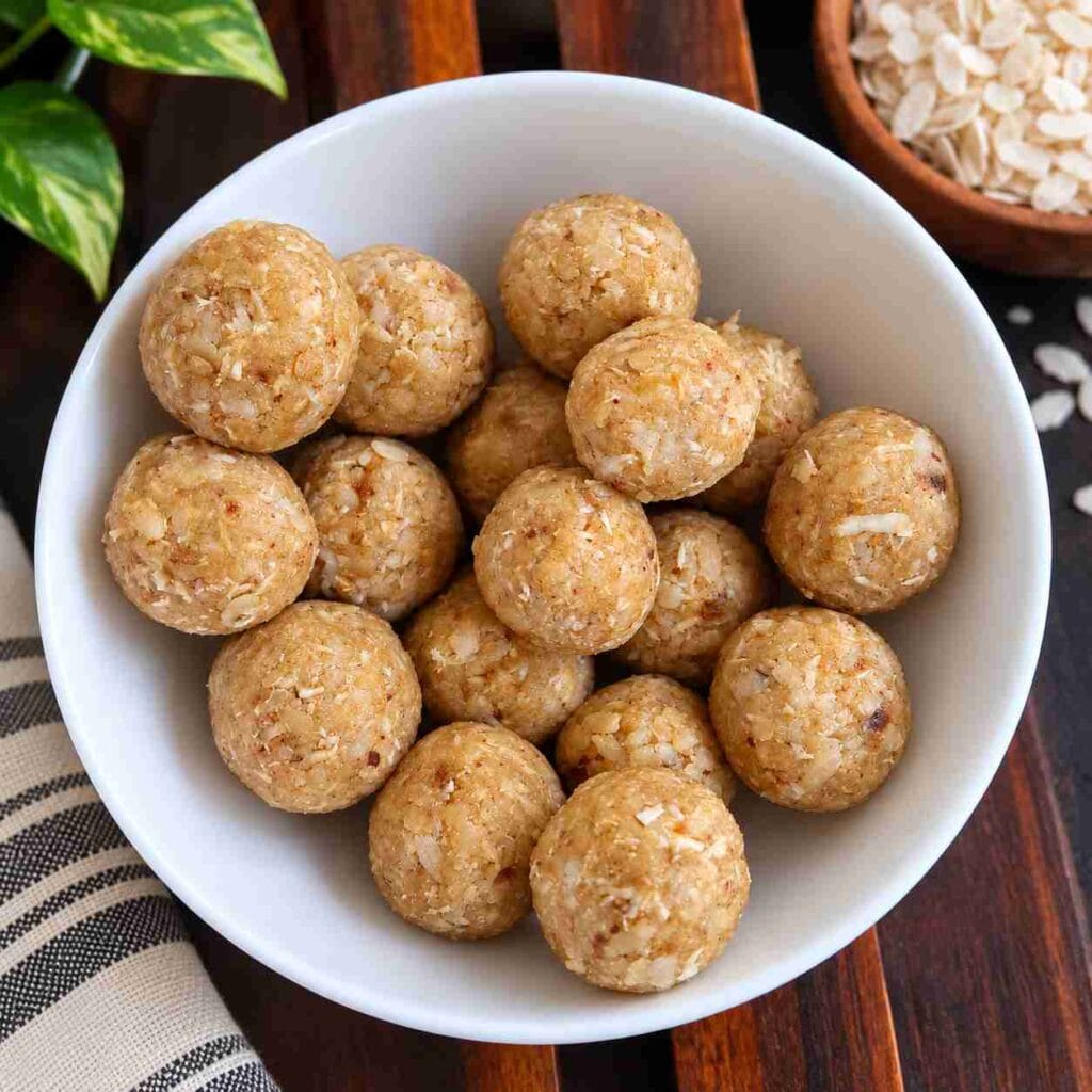 Bowl of round Aval Ladoo with coconut pieces, with poha visible in the background