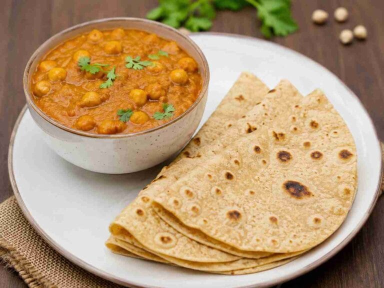 Bowl of chana masala served with folded chapathi on a white plate