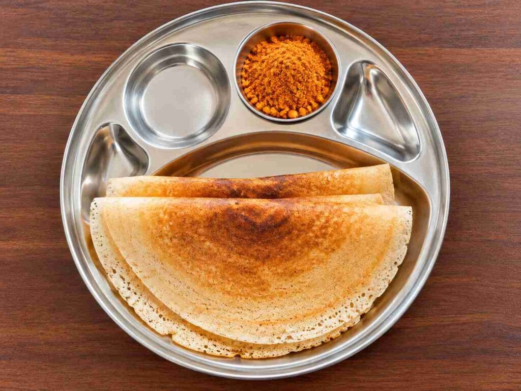 Golden crispy foxtail millet dosas folded and served on a steel plate